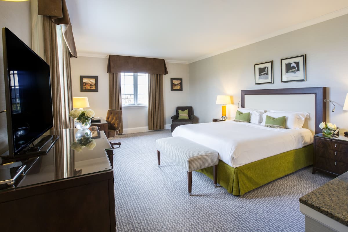 A hotel room with a large bed, a television, a desk with a lamp, and a window with curtains.