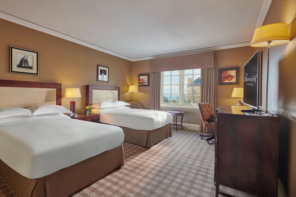A hotel room with two beds, a desk, a chair, a TV, and a window with a view.