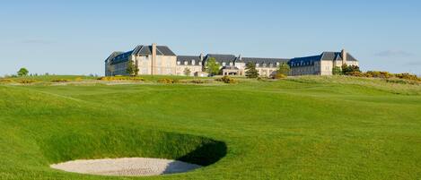 Un grand bâtiment à étages, doté d’une façade symétrique, situé sur une pelouse bien entretenue, avec un bunker de sable en premier plan.