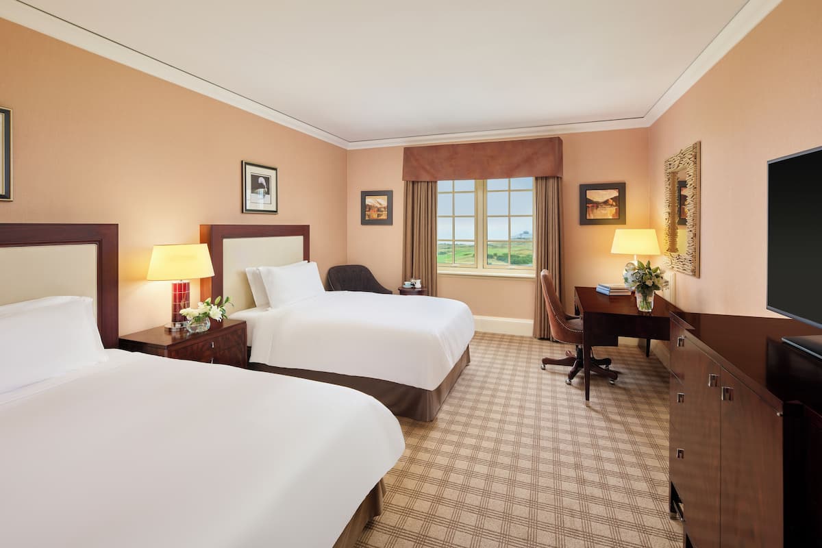 A hotel room with two beds, a desk, a chair, and a television.
