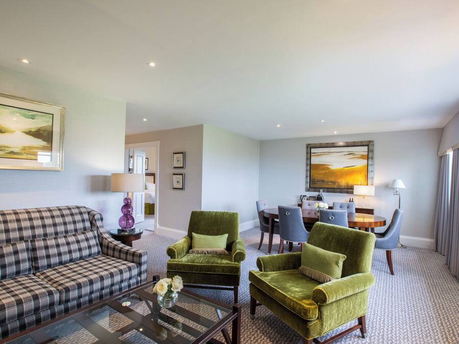 A modern living room with a sofa, armchairs, a coffee table, and a dining area with chairs and a table.
