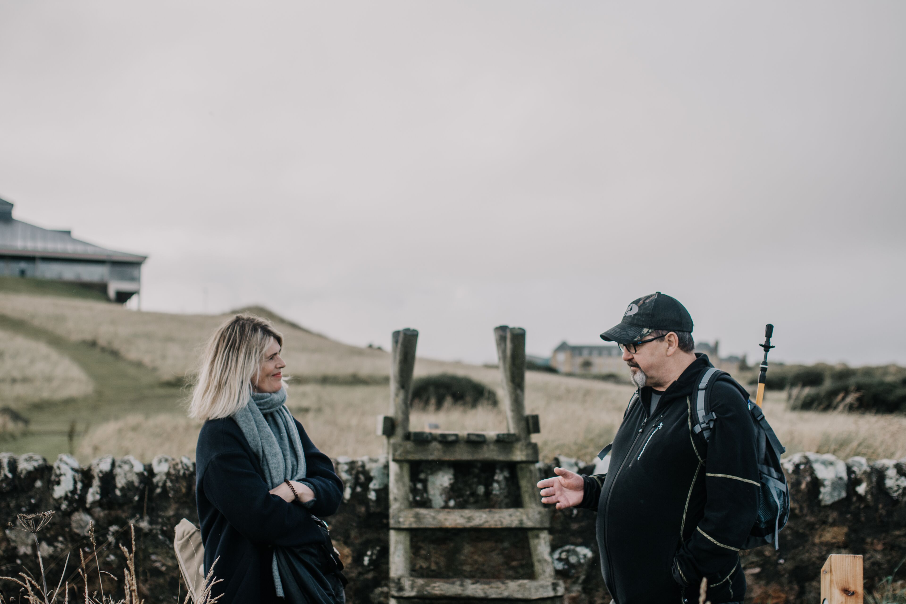 Two people standing in front of a stone wall with a wooden structure.