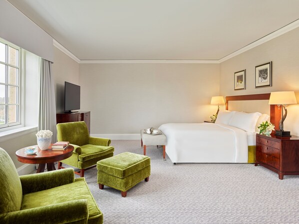 A hotel room with a bed, two green armchairs, a small table, a nightstand with a lamp, a TV, and a window with curtains. - Fairmont St Andrews (St. Andrews)