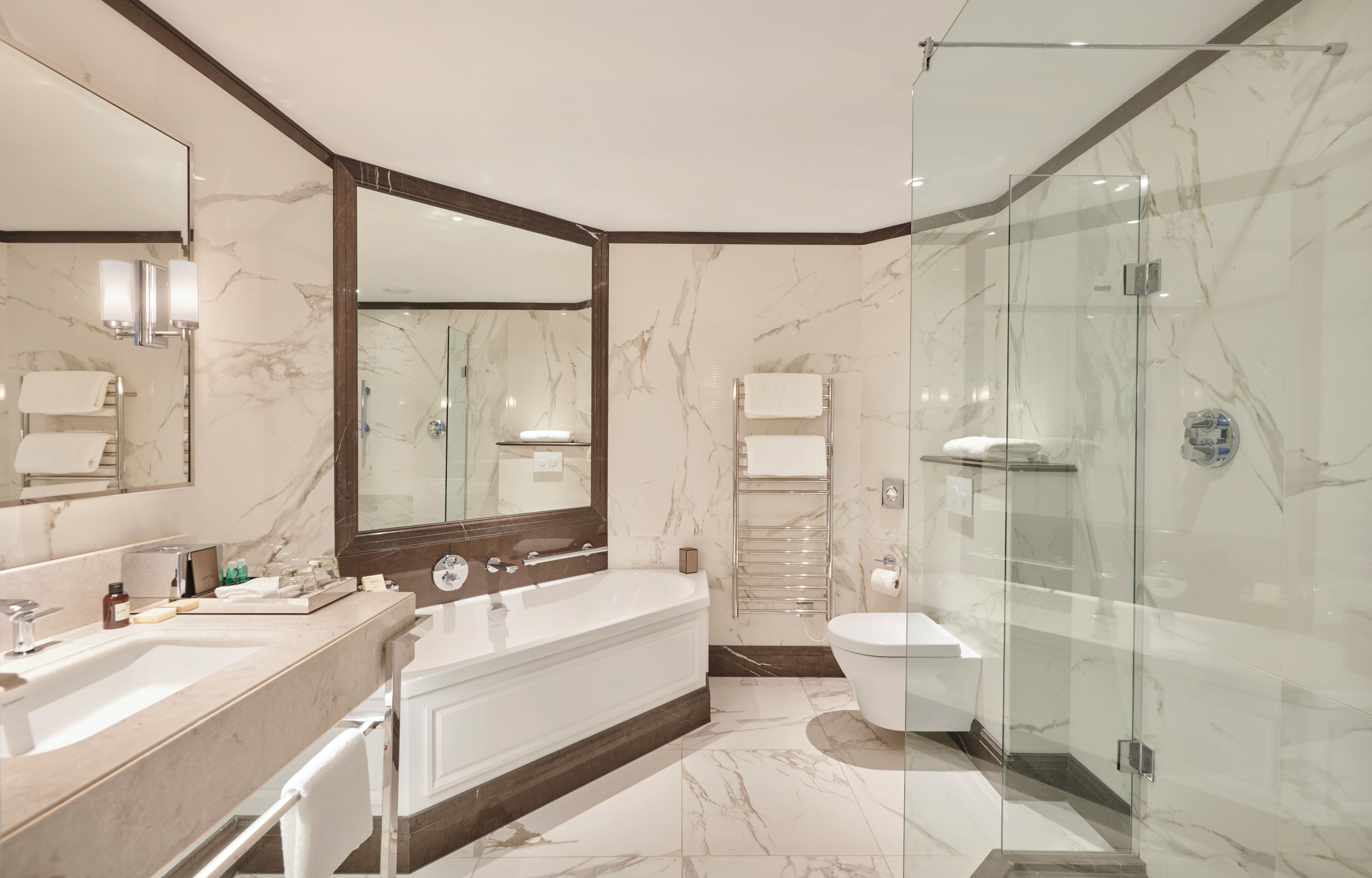 Un baño moderno con un espejo grande, una bañera, una ducha con mampara de vidrio y un inodoro.