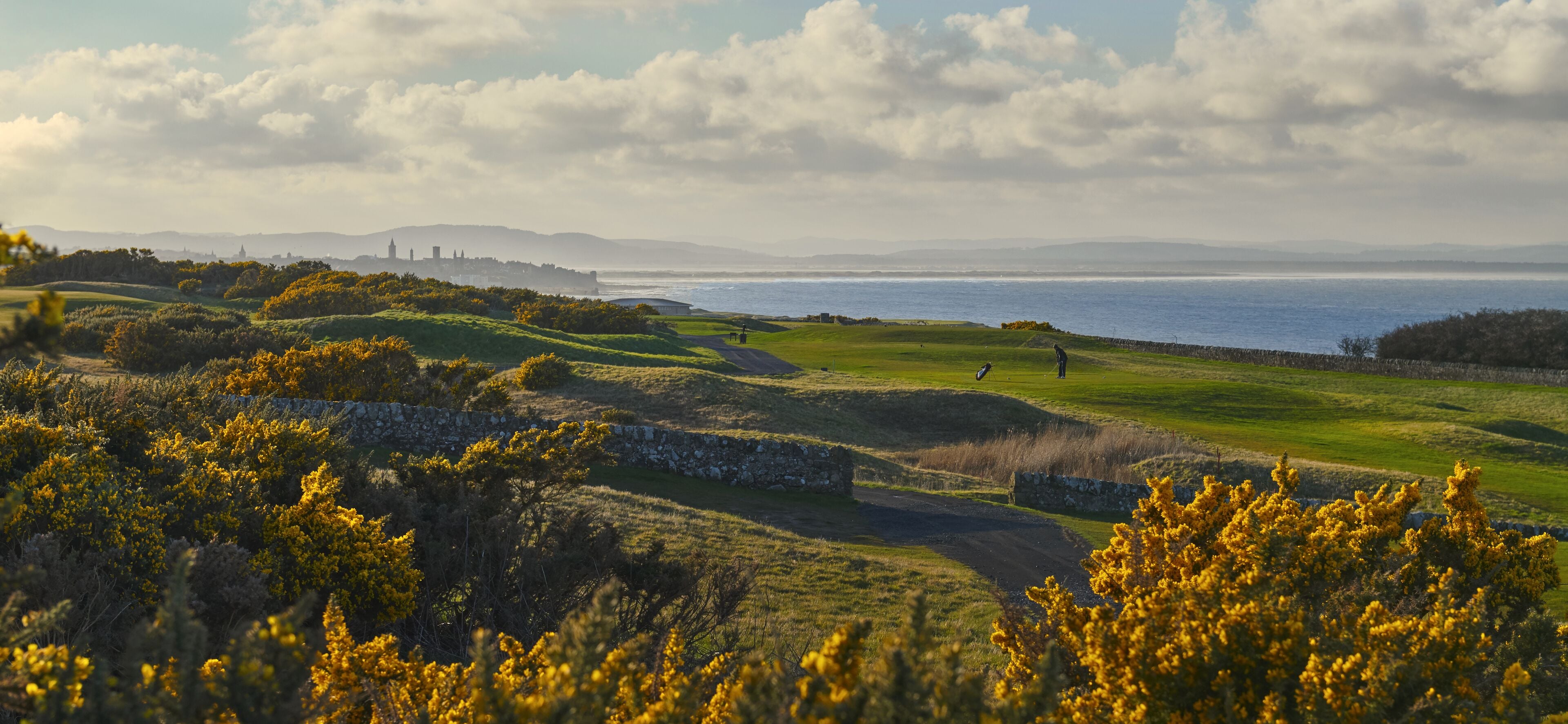 Un campo de golf con vistas al mar y colinas lejanas.