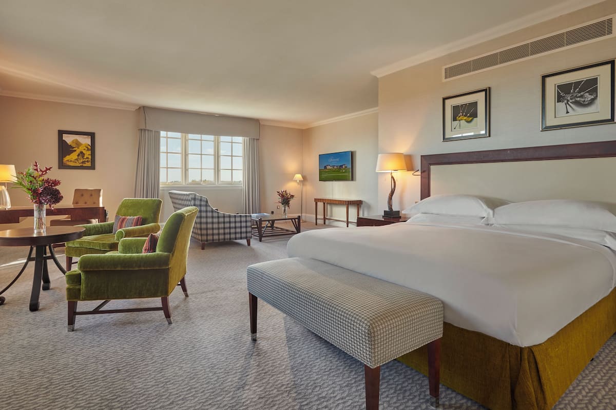 A hotel room with a large bed, two armchairs, a small table, and a desk.