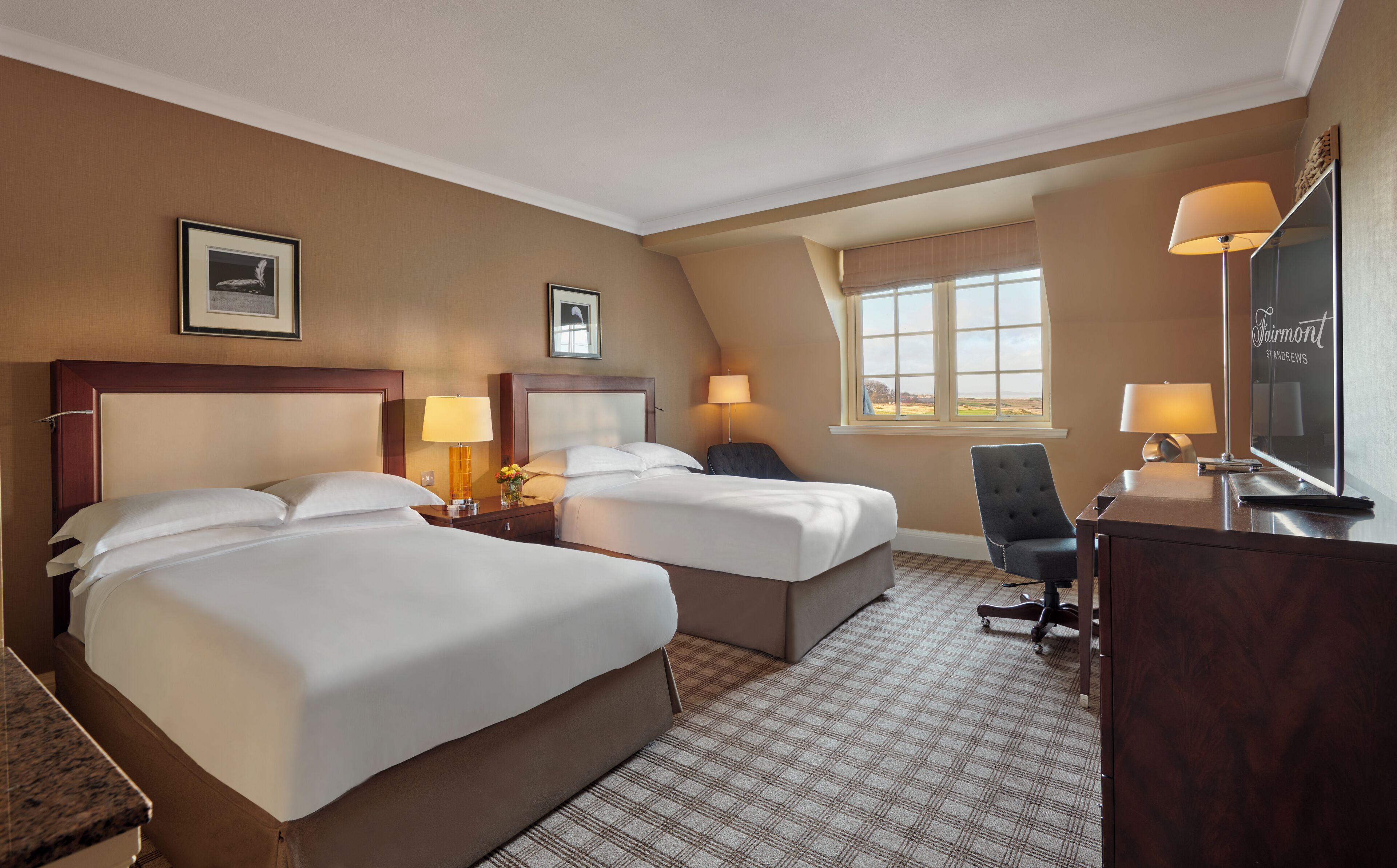 Een hotelkamer met twee bedden, een bureau, een stoel en een groot raam.