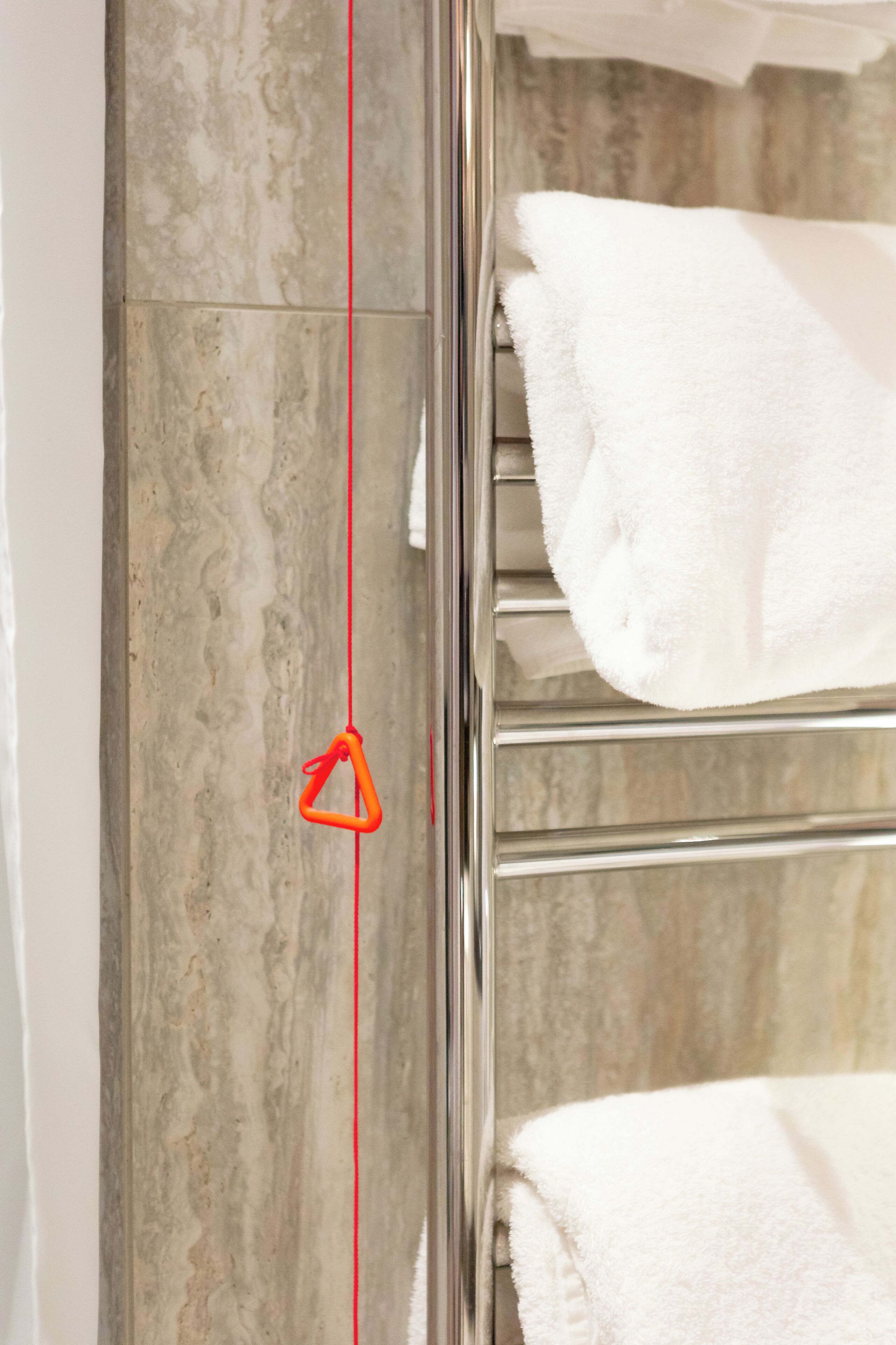 Une salle de bain avec un mur en marbre, un porte-serviettes chromé et un mètre ruban rouge.