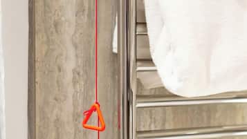 A bathroom with a marble wall, a chrome towel rack, and a red measuring tape.