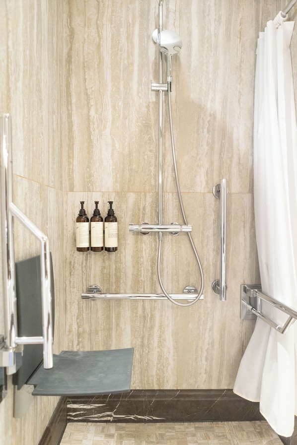 A shower area with a handheld showerhead, a wall-mounted faucet, and a glass-enclosed shower stall. There are three bottles of shampoo and conditioner on the wall. - Fairmont St Andrews (St. Andrews)