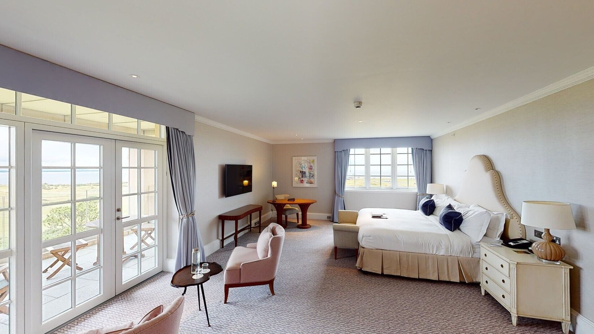 Ein Hotelzimmer mit großem Fenster, einem Bett, einem Schreibtisch, einem Stuhl und einem Fernseher.
