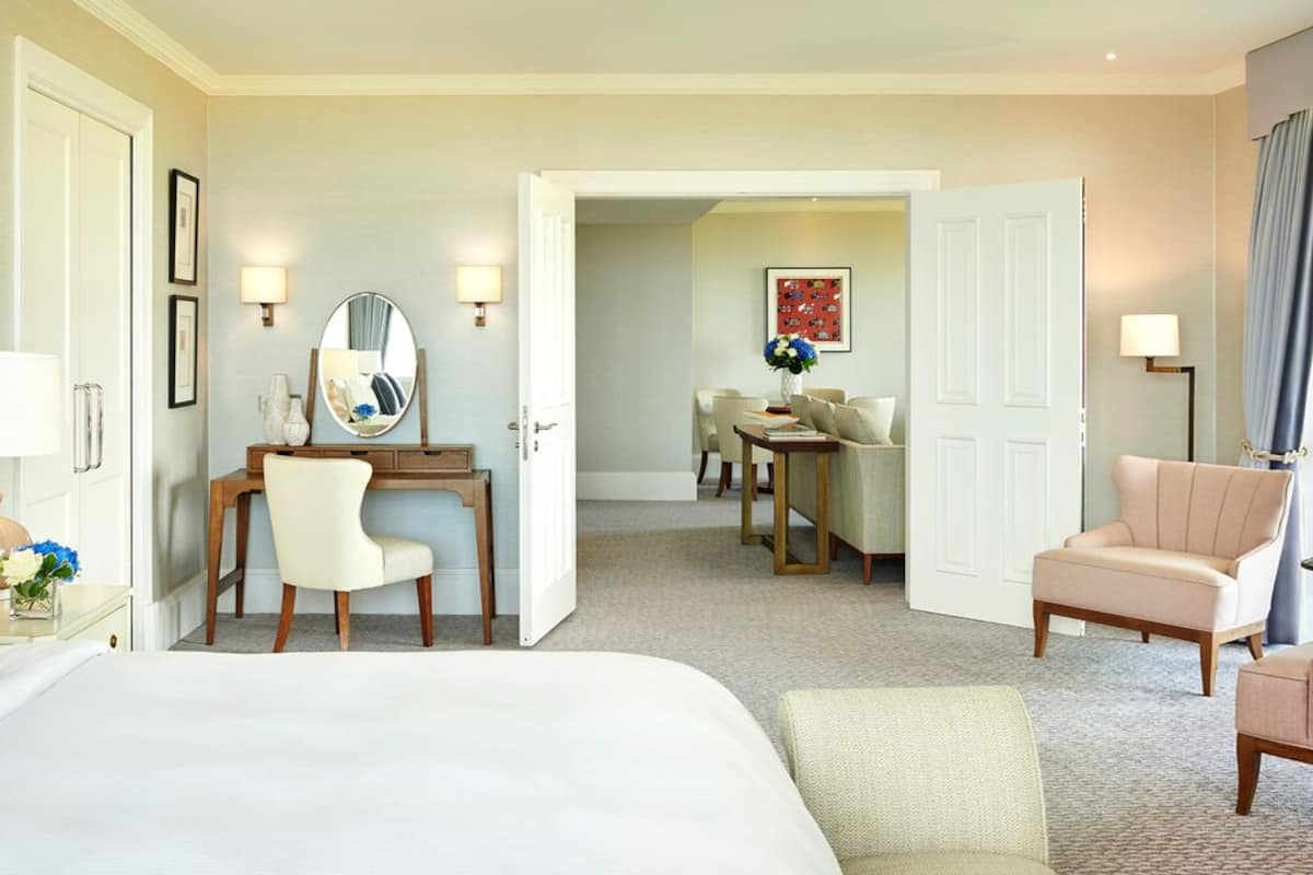 A hotel room with a large bed, a desk with a chair, a dining area with a table and chairs, and a sofa.