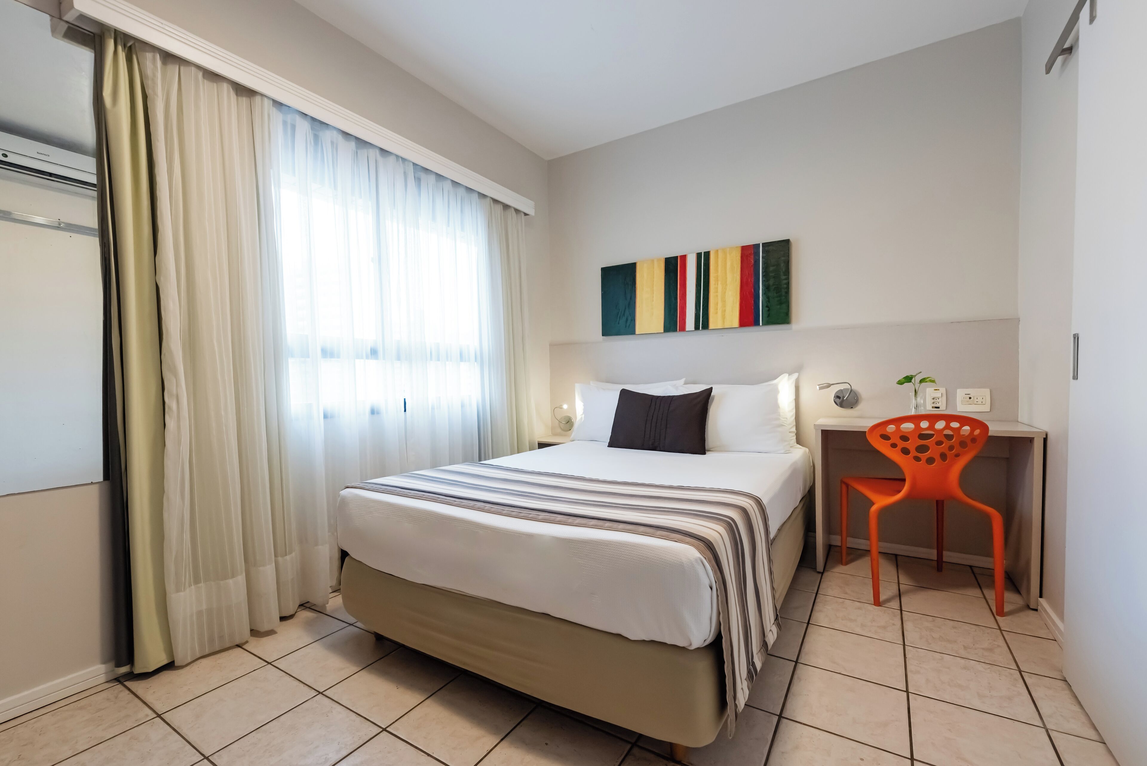 A hotel room with a bed, a desk, a chair, and a window with curtains.