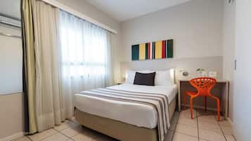 A hotel room with a bed, a desk, a chair, and a window with curtains.
