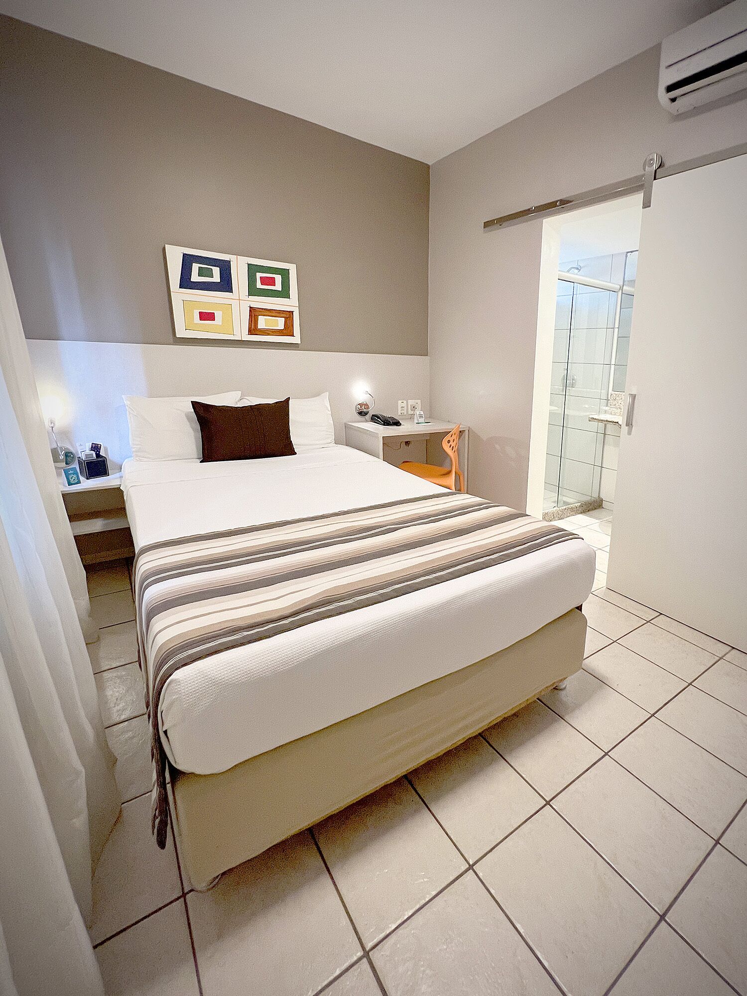 A modern hotel room with a large bed, bedside tables, a nightstand, a chair, and a shower area.