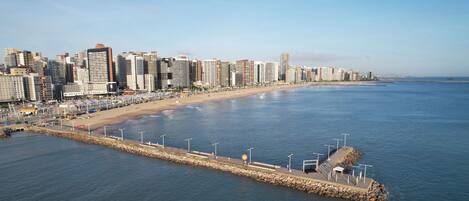 Un paisaje urbano costero con una playa extensa, un muelle de piedra y edificios altos.