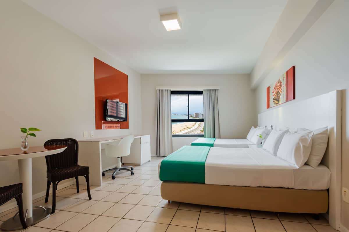 Een hotelkamer met een bed, bureau, stoel en uitzicht op het strand.