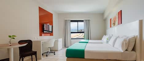 A hotel room with a bed, desk, chair, and a view of the beach.