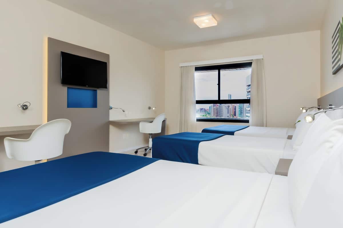 Een hotelkamer met twee bedden, een bureau, een stoel, een aan de muur bevestigde televisie en een raam met uitzicht over de stad.