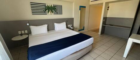 A hotel room with a large bed, bedside tables, a mirror, and a small desk.