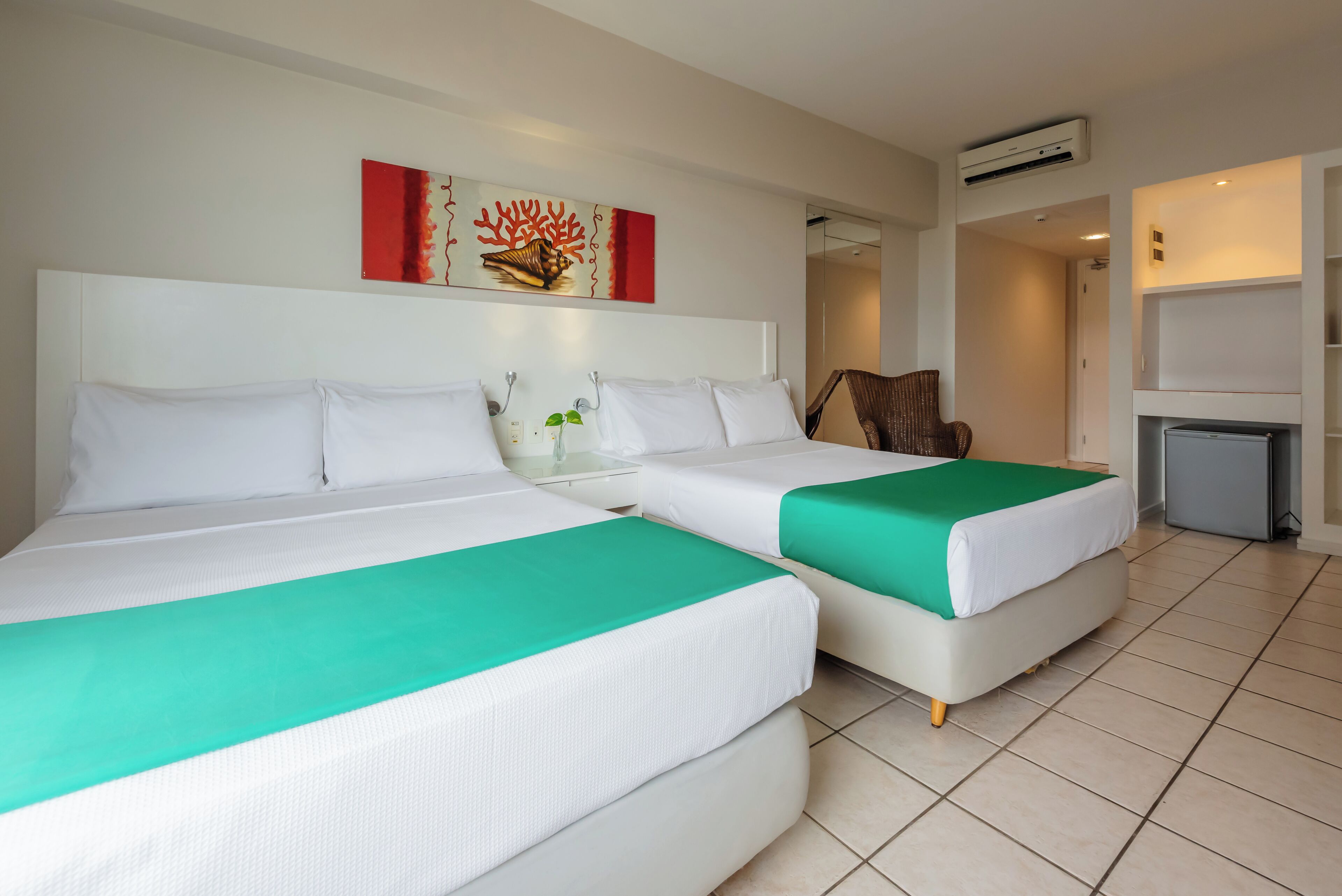 A hotel room with two beds, a small table with a plant, a chair, and a TV.