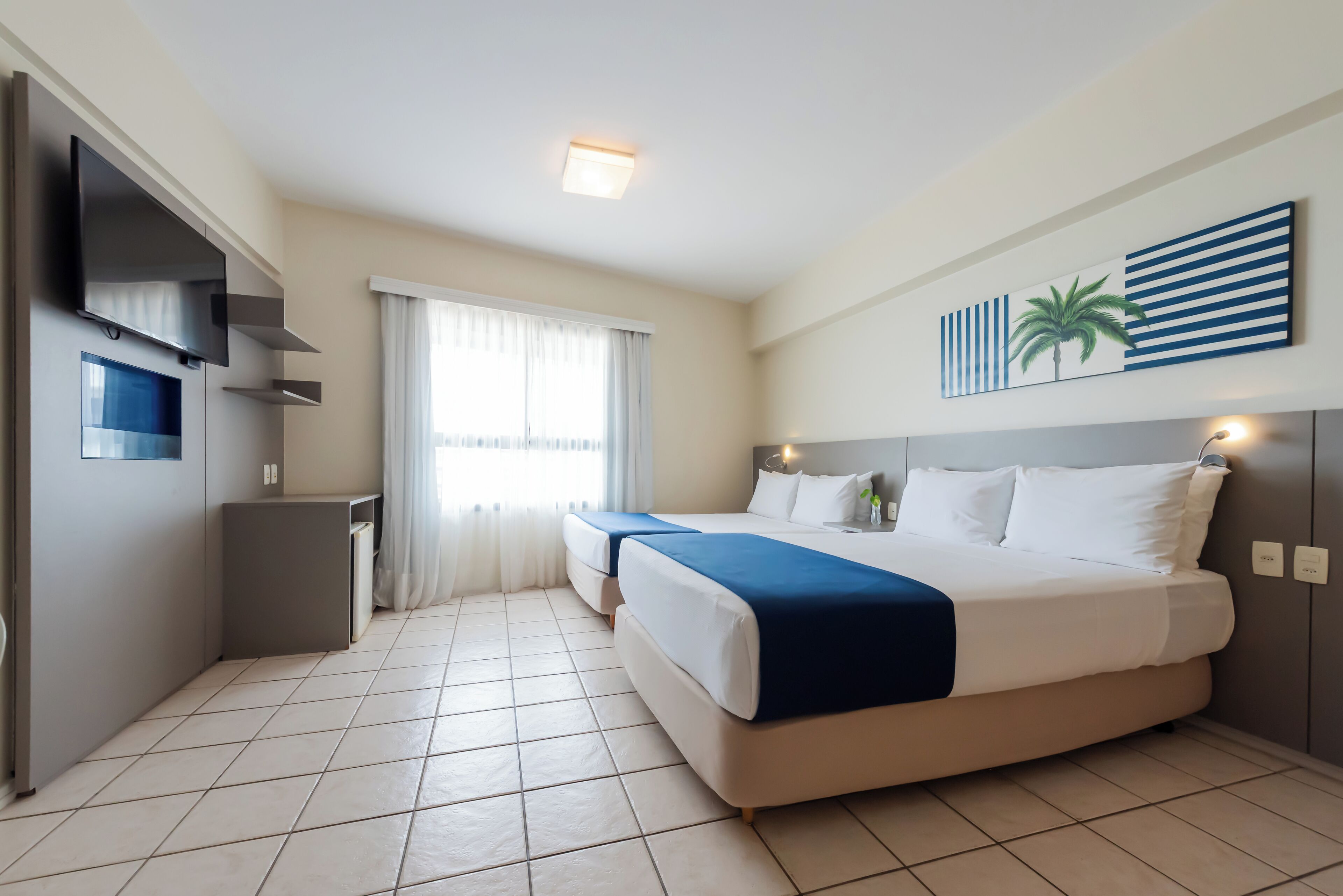 A hotel room with a large bed, a TV, a small desk, and a window with curtains.