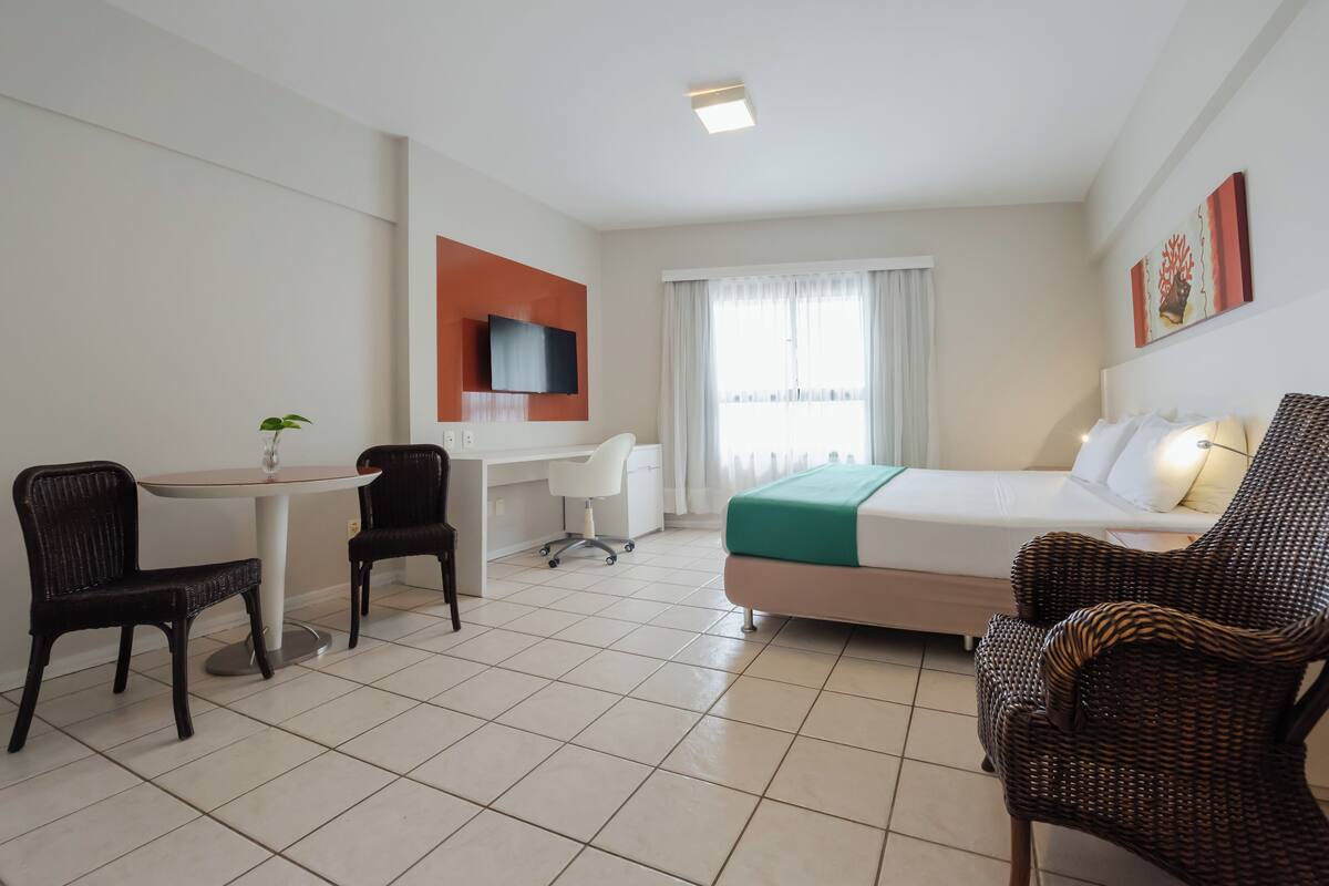 Een hotelkamer met een bed, een bureau, twee stoelen, een televisie en een raam met gordijnen.