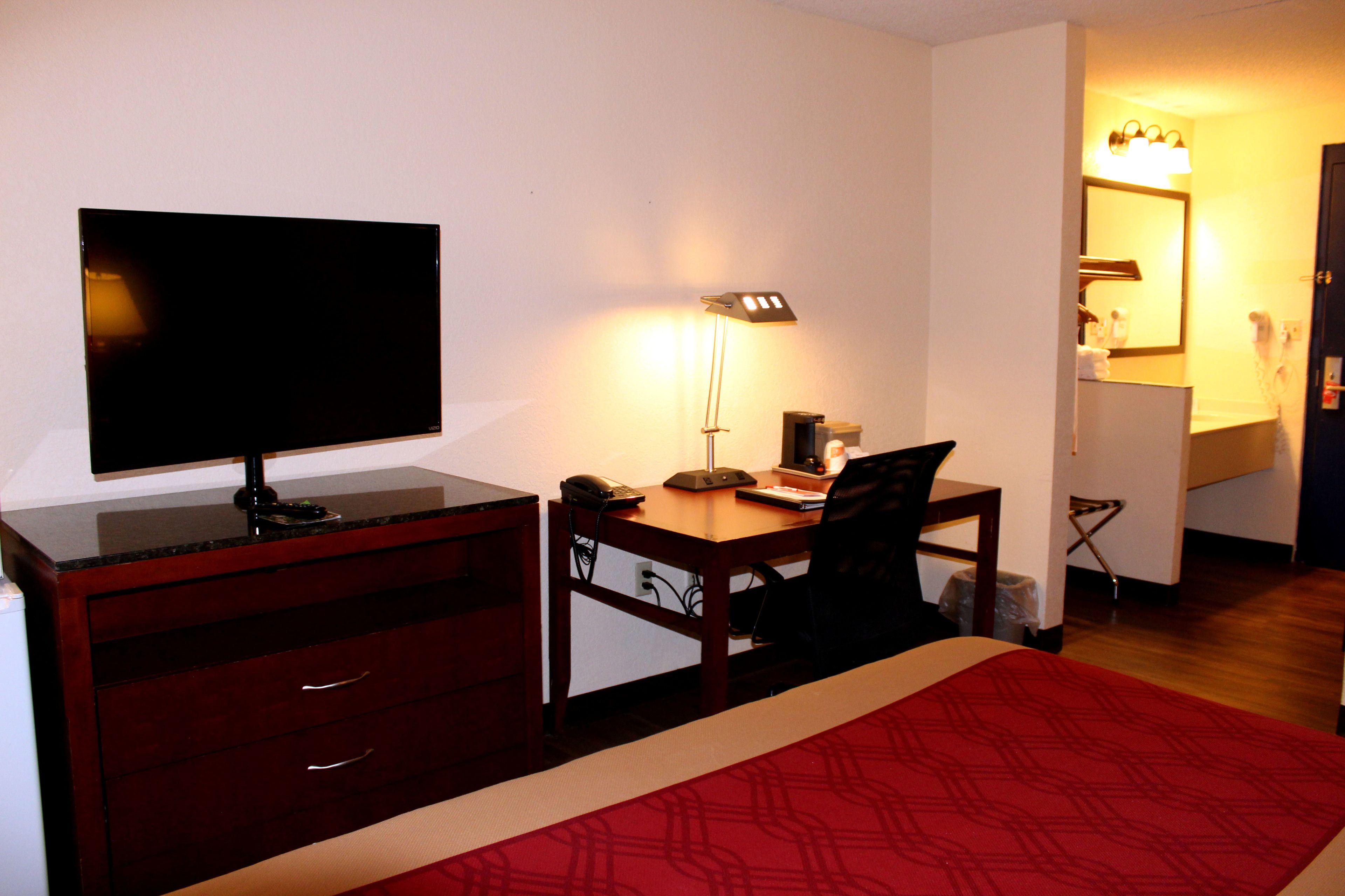 A hotel room with a bed, a desk with a computer, a TV, and a lamp.