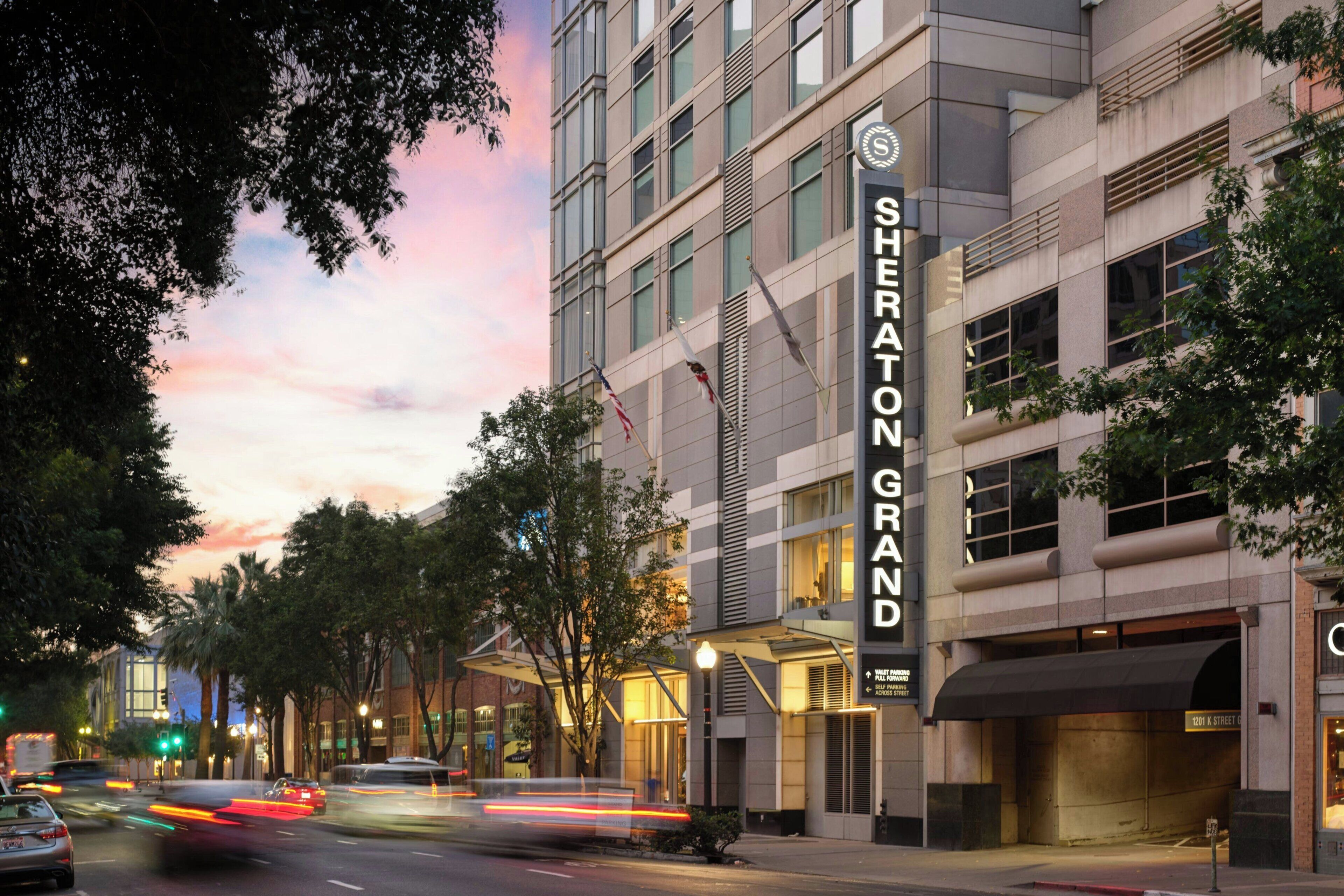 A hotel with a prominent sign, a street view, and trees.