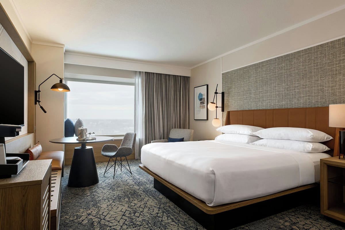 Ein Hotelzimmer mit einem großen Bett, einem Schreibtisch mit Stuhl, einem Fernseher und Blick auf die Stadt.