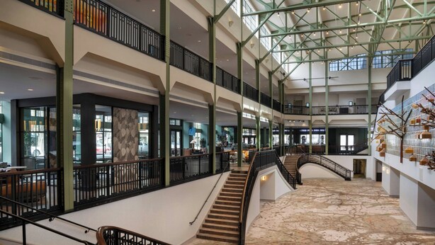 Un atrium à plusieurs niveaux, doté d’un escalier central, de rampes en verre et d’un sol à motifs.