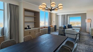 Une chambre d’hôtel moderne dotée d’un coin repas, d’un canapé, d’une grande fenêtre offrant une vue agréable et d’un lustre.