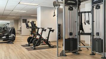 Ett gym med konditionsmaskiner, utrustning för styrketräning och en vägg med speglar.