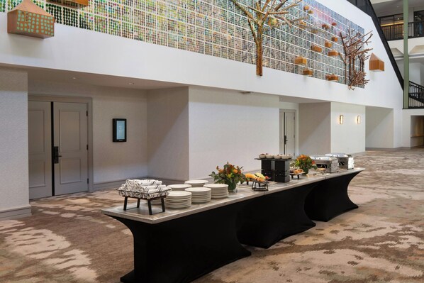 A spacious indoor area with a long buffet table, a high ceiling with a decorative tree, and a staircase in the background. - Sheraton Grand Sacramento Hotel (Sacramento)
