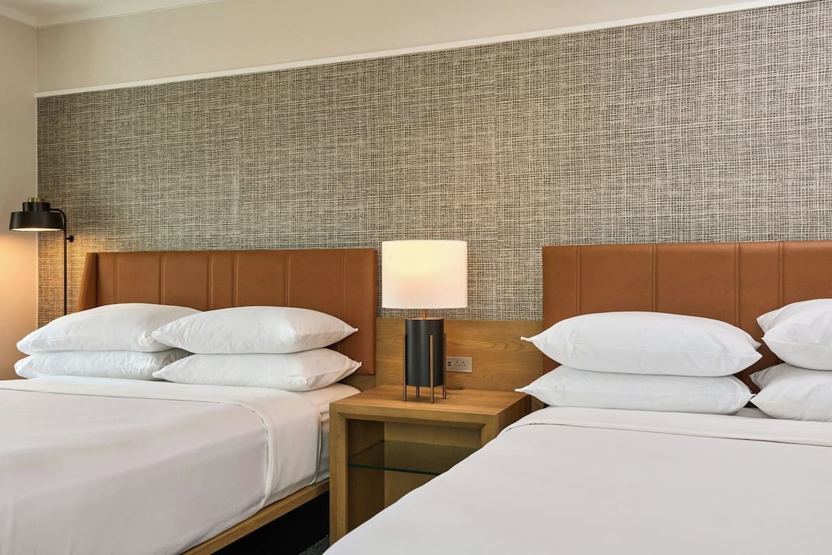 Ein Hotelzimmer mit zwei Betten, einem Holzkopfstück, einem Nachttisch mit Lampe und einer strukturierten Wand.