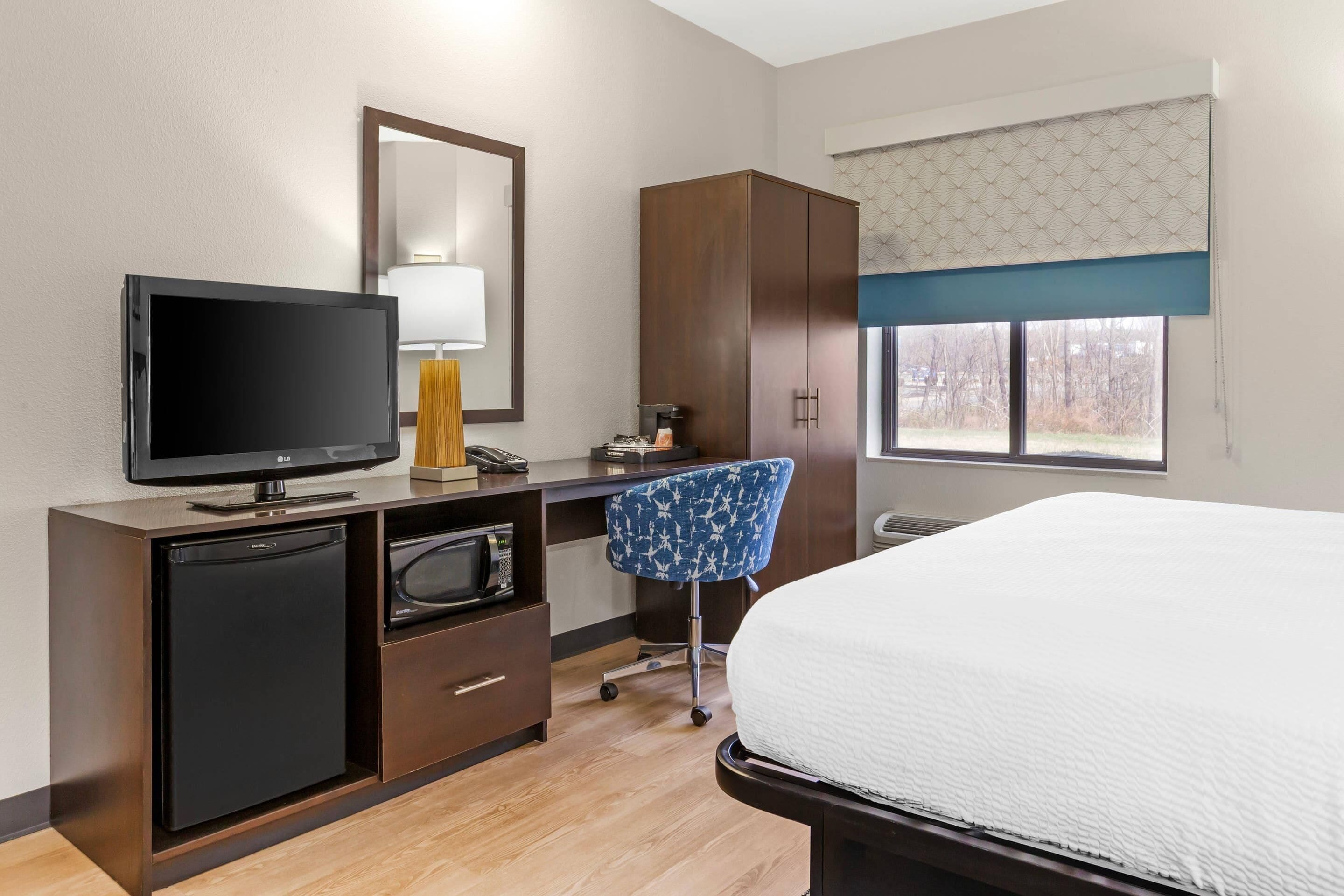A hotel room with a bed, a TV, a desk with a computer, a chair, and a wardrobe.