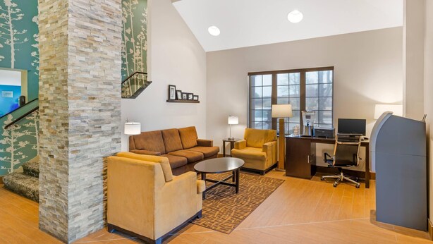 A spacious living area with a stone accent wall, a sofa, a coffee table, a desk with a computer, and a large window. - Sleep Inn Greensboro Airport (Greensboro)