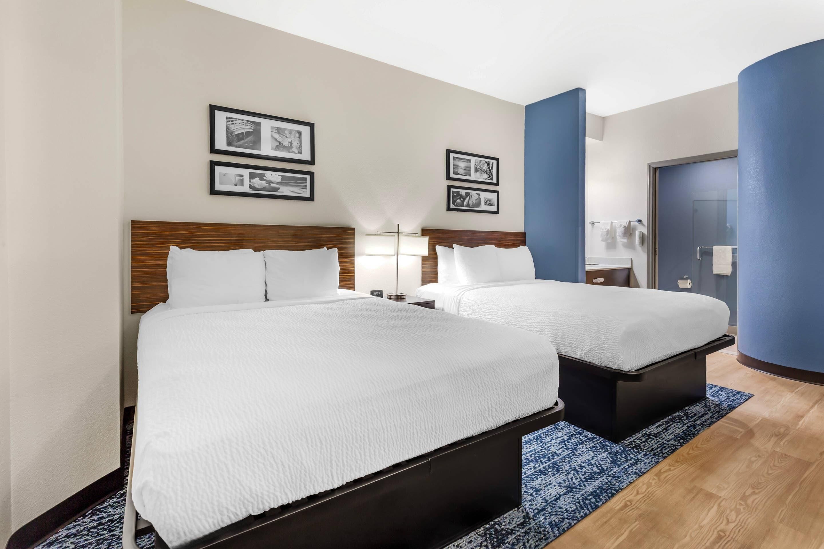 Habitación de hotel con dos camas, una pared de acento azul y cuadros en la pared.
