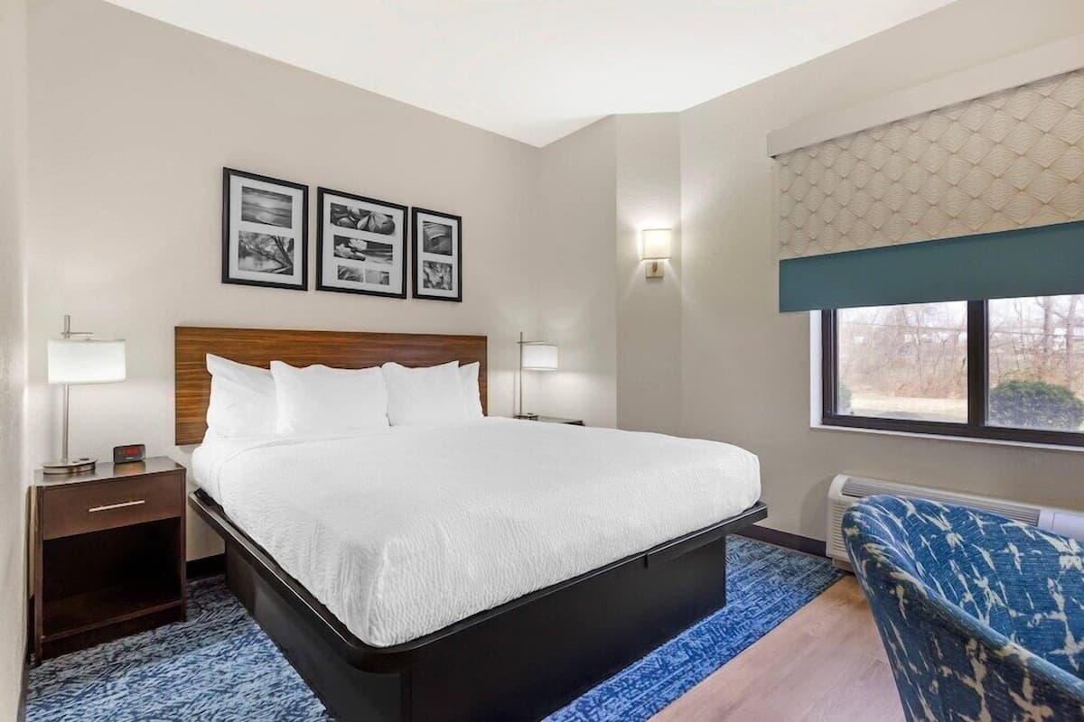 Une chambre d’hôtel avec un lit, des tables de chevet, une chaise, une fenêtre donnant sur un paysage agréable et des tableaux encadrés au mur.