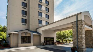 A multi-story hotel with a flat facade, large windows, and a covered entrance area with stone pillars. - Sleep Inn Greensboro Airport (Greensboro)