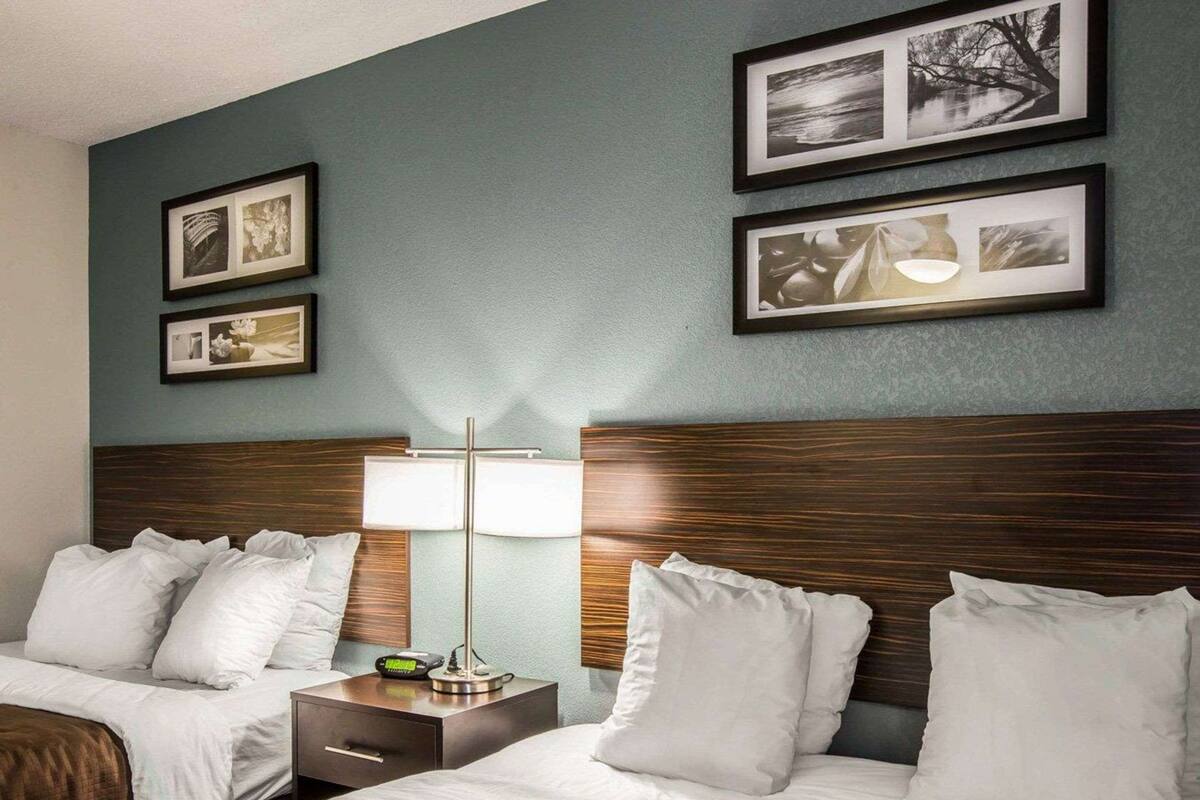 A hotel room with two beds, a nightstand with a lamp, and framed pictures on the wall.