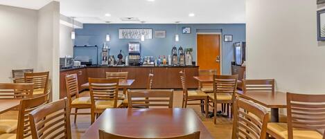 A dining area with wooden tables and chairs, a counter with coffee machines, and a blue wall with artwork.