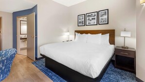A hotel room with a large bed, bedside tables with lamps, a blue chair, and a door leading to a bathroom. - Sleep Inn Greensboro Airport (Greensboro)