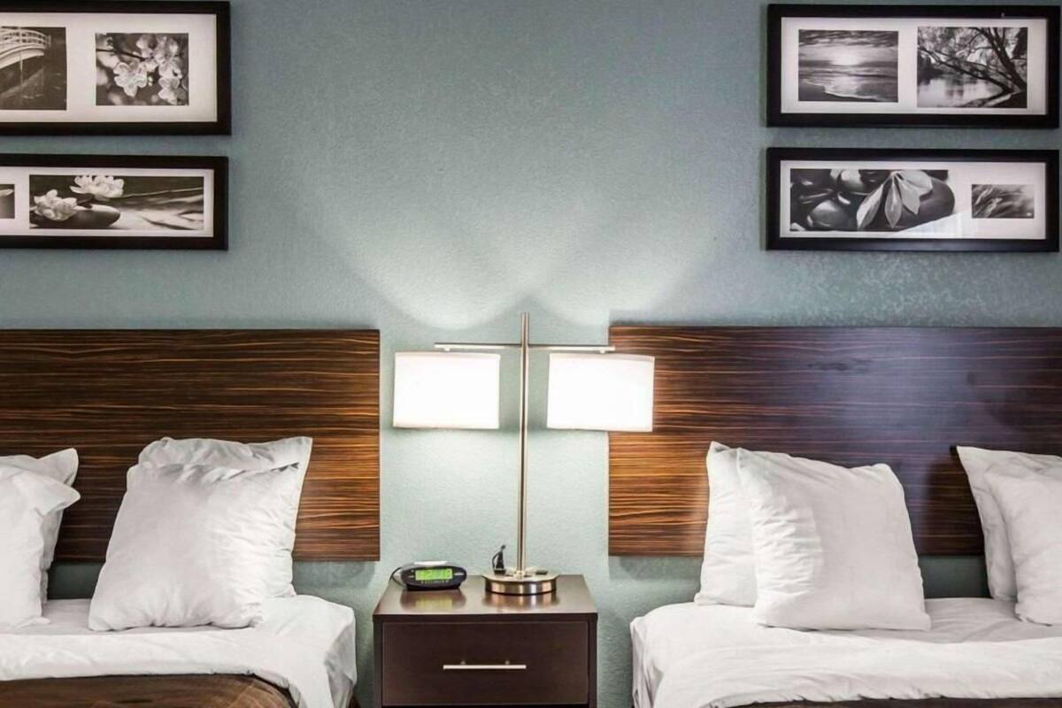 A hotel room with two beds, a nightstand with a lamp, and framed pictures on the wall.