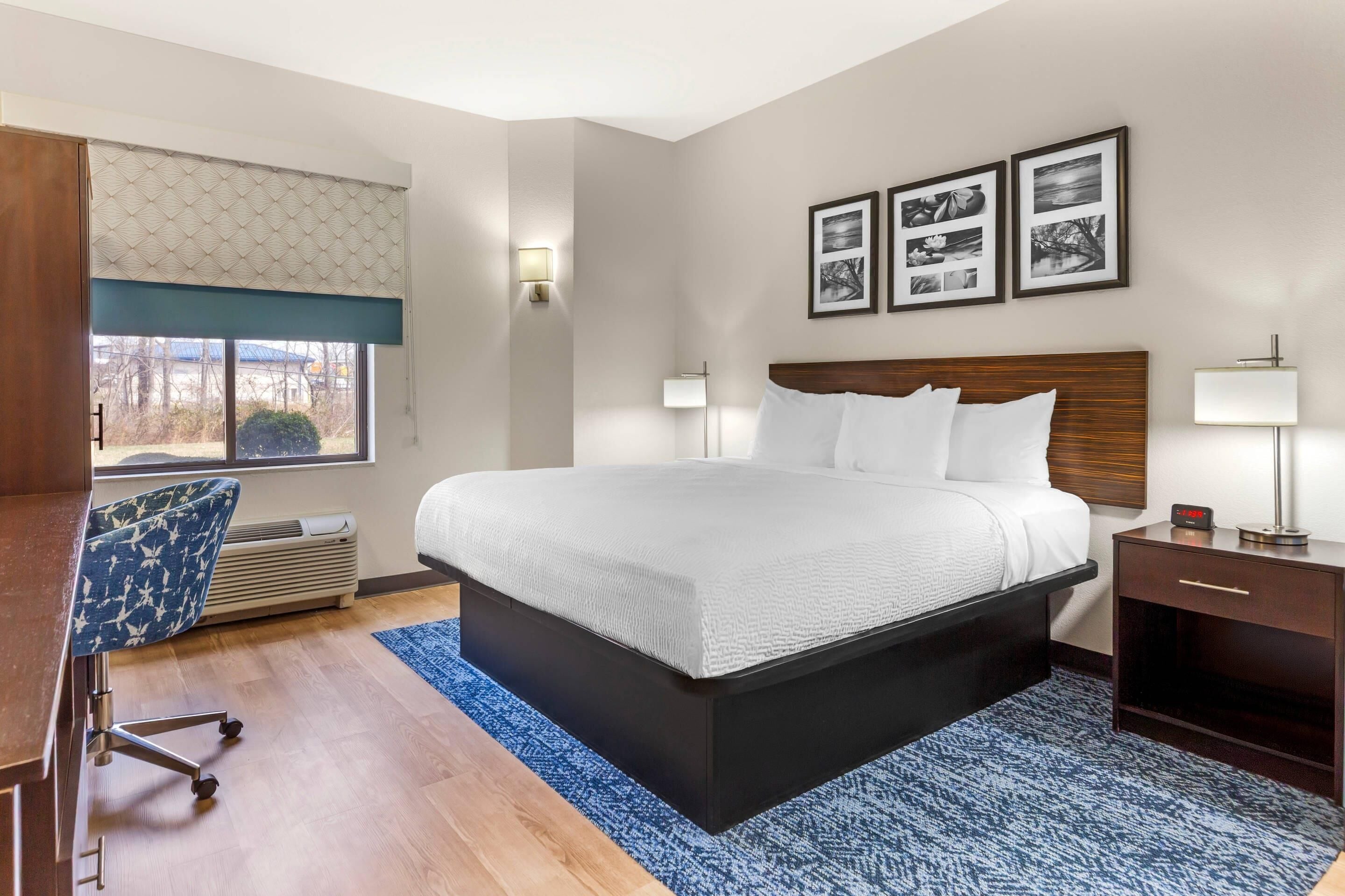 Une chambre d’hôtel avec un grand lit, un bureau avec une chaise, une table de chevet avec une lampe et une fenêtre donnant sur un beau paysage.