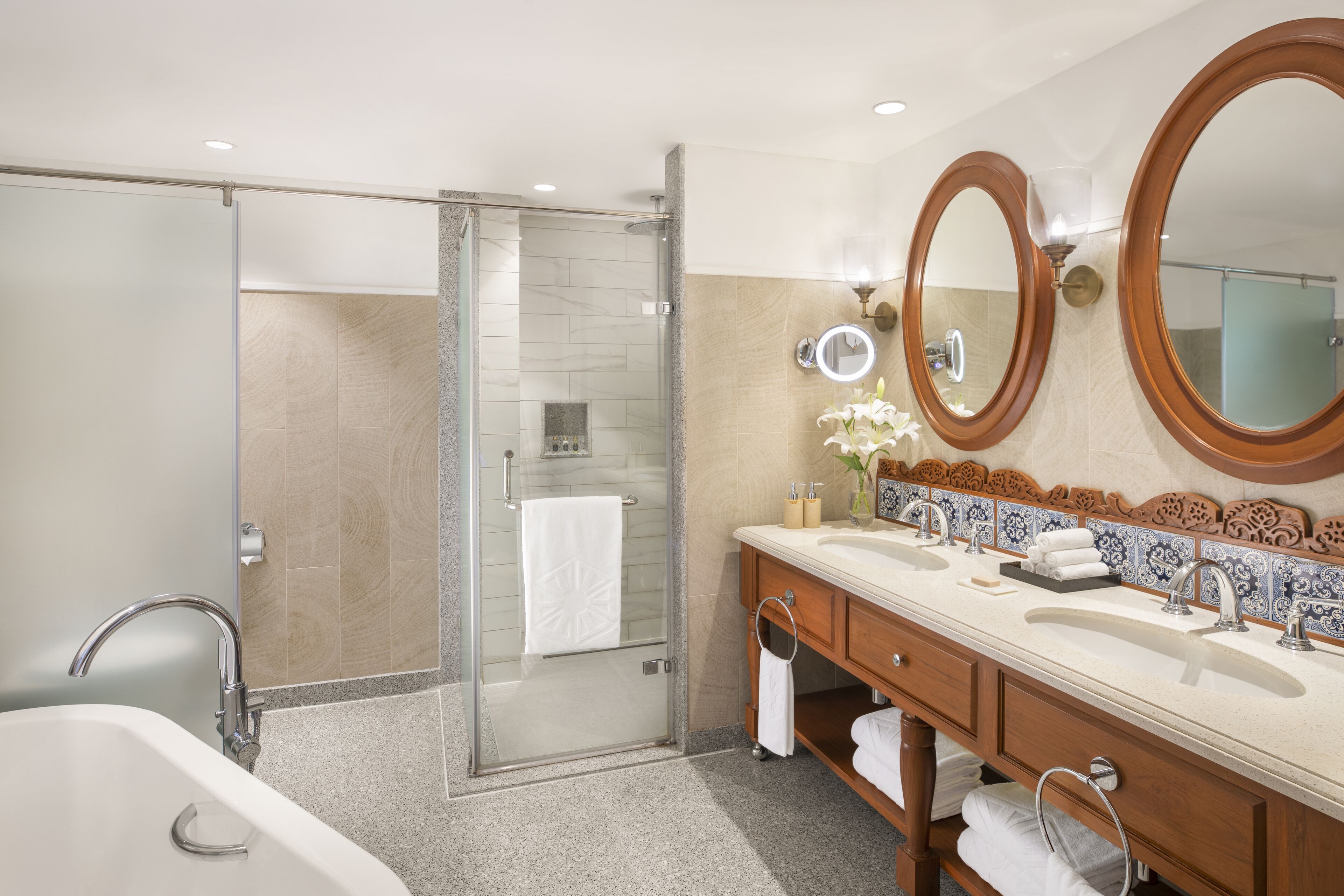 Un baño moderno con cabina de ducha de vidrio, un mueble de tocador grande con lavamanos dobles y dos espejos montados en la pared.