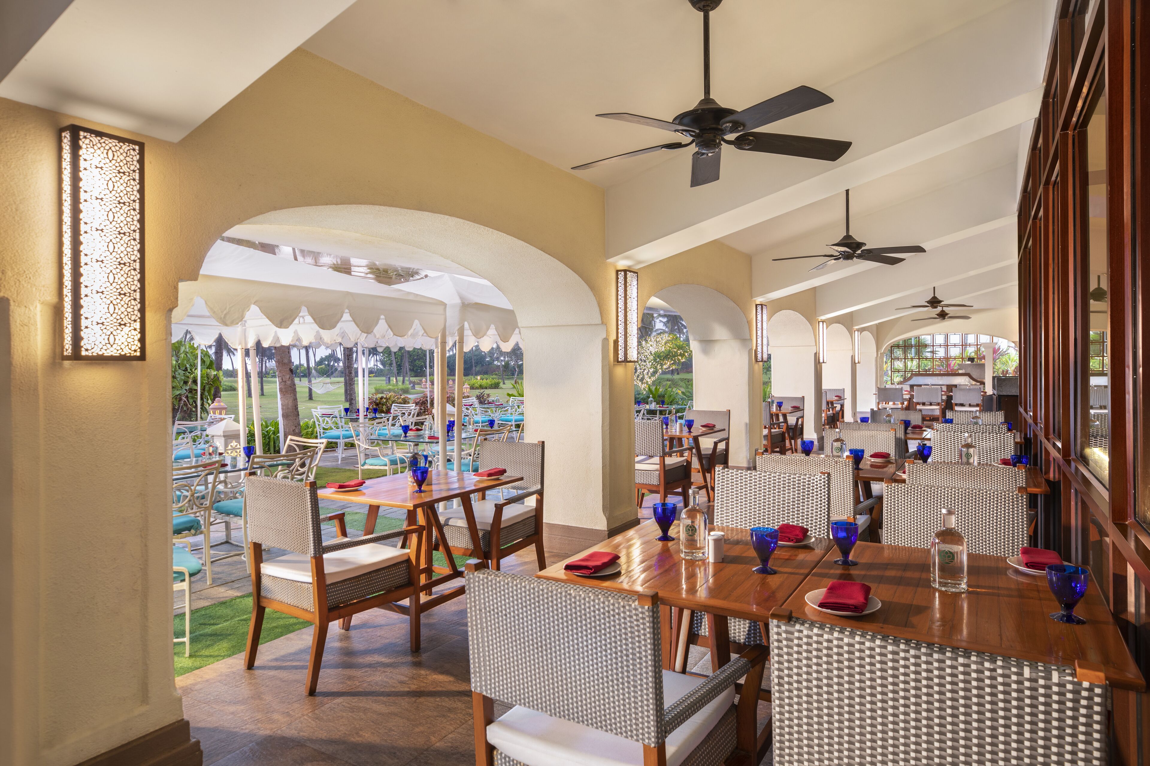 Un restaurante con terraza, sillas de mimbre blancas y mesas con servilletas rojas.