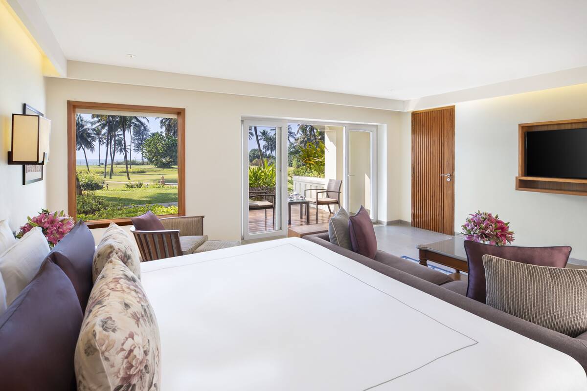 Un dormitorio amplio con una cama grande, un sofá, un televisor montado en la pared y un ventanal corredero que da a un espacio exterior con una mesa y sillas.