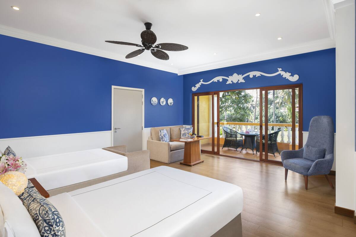 Una sala de estar moderna con una pared azul de acento, un ventilador de techo, un sofá, una silla y vistas al exterior a través de un ventanal corredera.