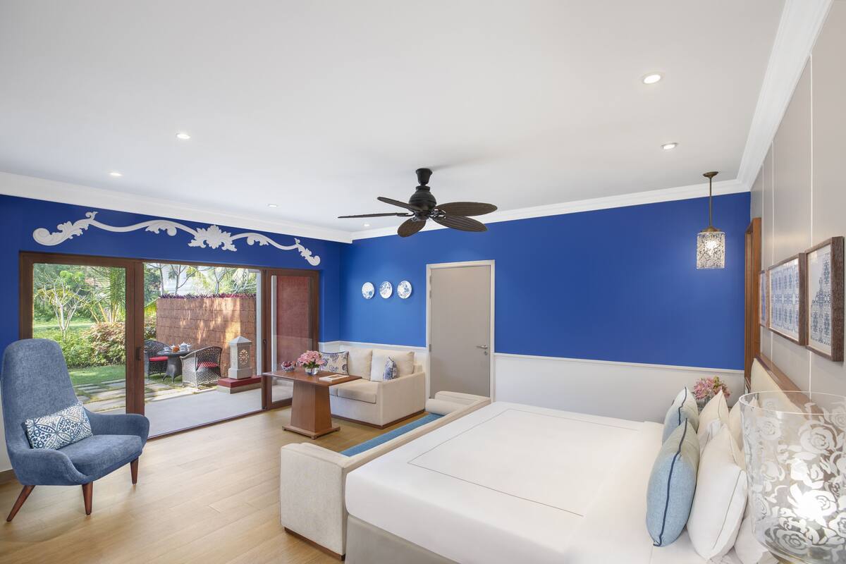 Una habitación moderna con una pared azul de acento, un ventilador de techo, un sofá blanco, un sillón azul y un comedor con mesa y sillas.